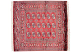 Cherry red Bokhara rug corner: detailed gul medallions, intricate borders, and ivory fringe.