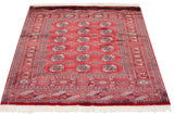 Bokhara rug corner showcasing cherry red field, navy gul medallions, and ivory fringe.