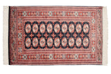 Corner of a vintage Bokhara rug showing the fine weave, geometric borders, and intact side cord.