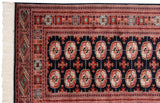 Corner of a fine vintage Bokhara rug, showing detailed geometric borders and neat ivory fringe.