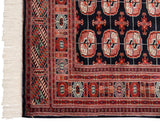 Corner of a vintage Bokhara rug showing its multi-layered geometric borders and clean ivory fringe.