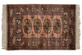 Vintage Bokhara rug corner with dusty rose geometric motifs and ivory fringe.
