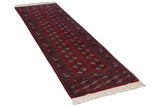 Angled view of a fine Bokhara runner with repeating gul medallions on a cherry red field and ivory fringe.