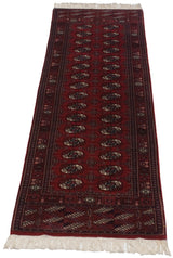 Angled perspective of a vintage Bokhara runner with repeating red, navy, and ivory guls.