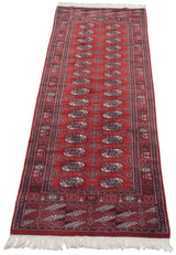 Angled view of a vintage Bokhara runner showing repeating gul medallions on a cherry red field.