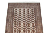 Angled view of a vintage Bokhara carpet's plush pile, intricate geometric border, and soft fringe.