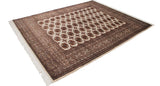 Angled view of a vintage Bokhara carpet's repeating gul pattern in coffee brown and ivory.