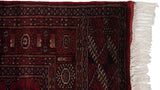 Corner of a vintage Bokhara rug showing the intact side cord, tight weave, and clean ivory fringe.
