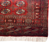 Corner of a fine Bokhara rug highlighting the cherry red gul medallions, detailed borders, and ivory fringe.