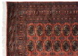 Bokhara carpet corner, white fringe, intricate geometric borders, and dusty rose gul medallions.