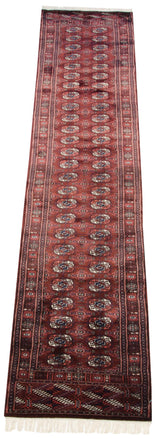 Angled view of a lustrous vintage Bokhara runner with repeating red and navy gul medallions.