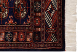 The corner of a vintage Bokhara rug with detailed navy and rust gul medallions, intact side cord, and ivory fringe.