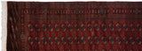 Corner of a vintage Bokhara rug showing its intricate red borders, selvage, and ivory fringe.