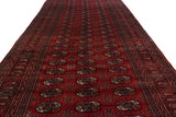 Perspective view down the length of a vintage Bokhara runner with repeating cherry red gul medallions.