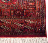 End corner of a vintage Bokhara runner with geometric borders, a red kilim, and clean ivory fringe.