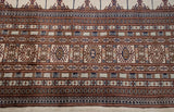 Detailed border of a fine Bokhara carpet, showing geometric gul medallions in bronze, navy, and copper.