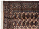 Corner of a Vintage Bokhara carpet showing intricate navy and bronze gul medallions on a beige field.