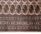 Detail of plush vintage Bokhara carpet pile: beige field, navy gul medallions, and seafoam border.