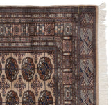 Vintage Bokhara carpet corner: beige, navy gul medallions, patterned border, and white fringe.