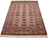 A vintage Bokhara rug seen at an angle, showing the lustrous sheen on its repeating gul pattern.