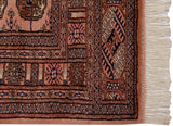 Corner of a vintage Bokhara rug showing the plush dusty rose pile, detailed border, and intact fringe.