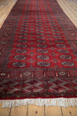 Angled view of a fine Bokhara runner showing its lustrous red pile and repeating navy gul medallions.