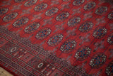 Angled view showing the plush red pile, intricate border, and gul medallions of a Bokhara rug.