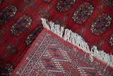 A folded corner of a Bokhara runner shows its plush red pile and fine, hand-knotted foundation.