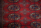 Finely woven gul medallions in navy and ivory on the plush red wool of a vintage Bokhara rug.