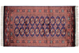 Vintage fine Bokhara rug with repeating gul medallions in chestnut rust and ivory on a navy blue field.