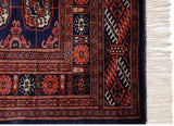 Detailed corner of a vintage Bokhara rug showing intact navy selvage and full ivory fringe.