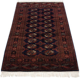 A vintage Bokhara rug viewed from a long angle, displaying its full geometric pattern.