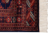 Plush navy wool, rust-colored geometric patterns, and ivory fringe on a vintage Bokhara rug corner.