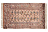 Vintage Bokhara rug with dusty rose field, elephant footprint gul medallions, navy and bronze tones.