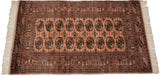 Bokhara rug corner showing intricate geometric border, original fringe, and dusty rose gul medallions.