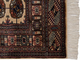 Corner of a vintage Bokhara rug showing the fine weave, detailed geometric borders, and ivory fringe.