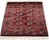 Wine red Bokhara rug end with repeating gul medallions, geometric borders, and ivory fringe.