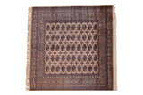 Vintage Bokhara square rug with repeating elephant footprint guls in camel, navy, and terracotta.