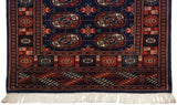 The geometric terminal border in chestnut rust and navy blue, showing the plush pile and ivory fringe of a Bokhara rug.