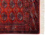 Intricate copper and navy border design meeting the full ivory fringe on a vintage Bokhara rug corner.