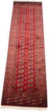 Plush cherry red Bokhara runner end, showcasing ivory fringe, detailed borders, and navy gul medallions.