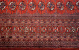 Detail of the Bokhara carpet's intricate borders and repeating gul medallions in red and navy blue.