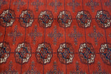 Detailed view of repeating gul medallions in navy and ivory on a plush, brick red wool pile.