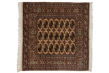 Vintage Bokhara square rug with repeating elephant footprint guls in navy blue and bronze on a beige field.
