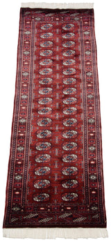 Angled view of a vintage Bokhara runner showing its repeating gul pattern on a wine red field.