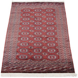 Vintage Bokhara carpet from an angle, displaying the lustrous sheen on its red geometric pattern.