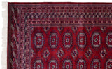 Clean ivory fringe and intricate geometric border on the corner of a vintage wine-red Bokhara carpet.