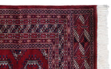 A vintage Bokhara carpet's corner with intricate geometric borders and original full white fringe.