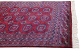 Angled corner view of a vintage Bokhara rug, detailing the geometric border and plush ivory fringe.