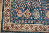 Pakistani Caucasian rug corner: indigo field, ivory border, red, green, peach geometric motifs, and fringe.